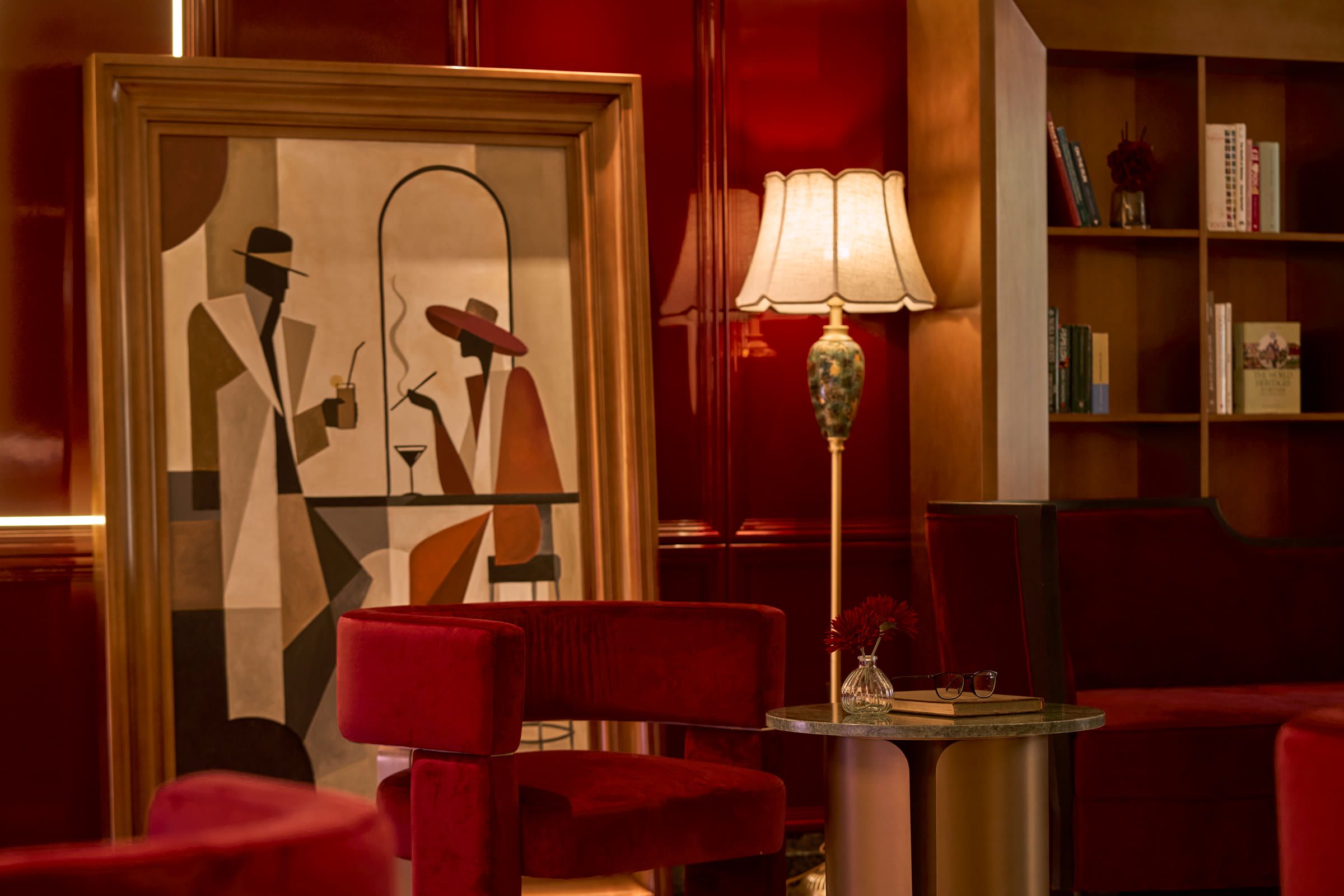 Red velvet armchairs and a floor lamp beside an art deco painting, against red lacquer walls.