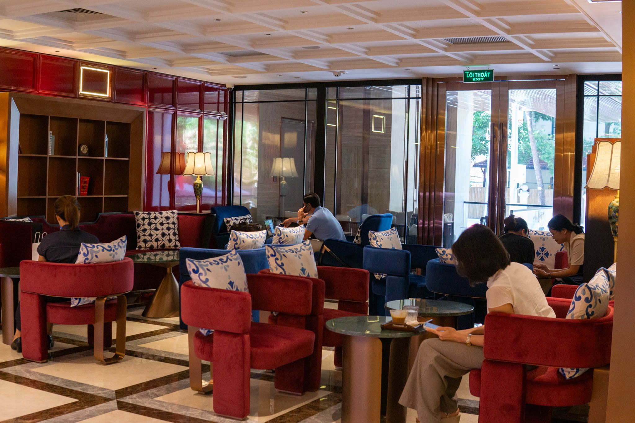 Guests sit in red and navy velvet chairs with blue-and-white cushions, in front of a bookshelf and glass doors.