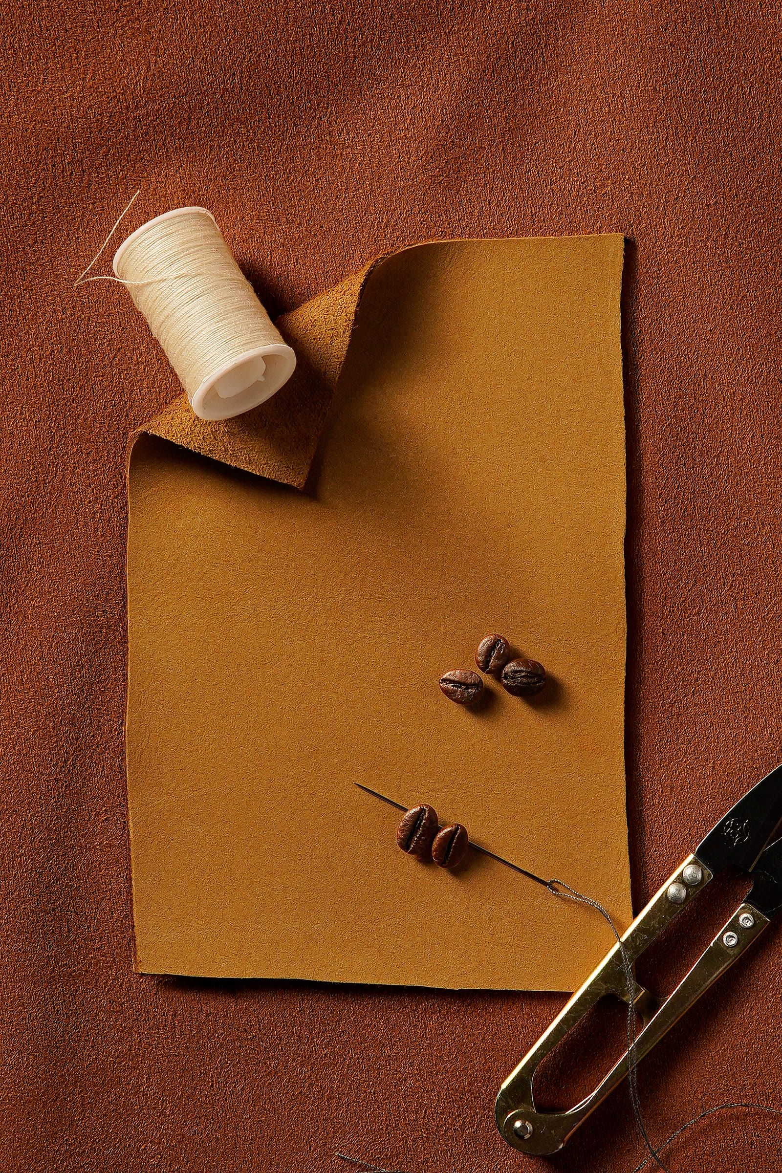 A piece of kraft fabric with coffee beans, a needle and thread, and small scissors.