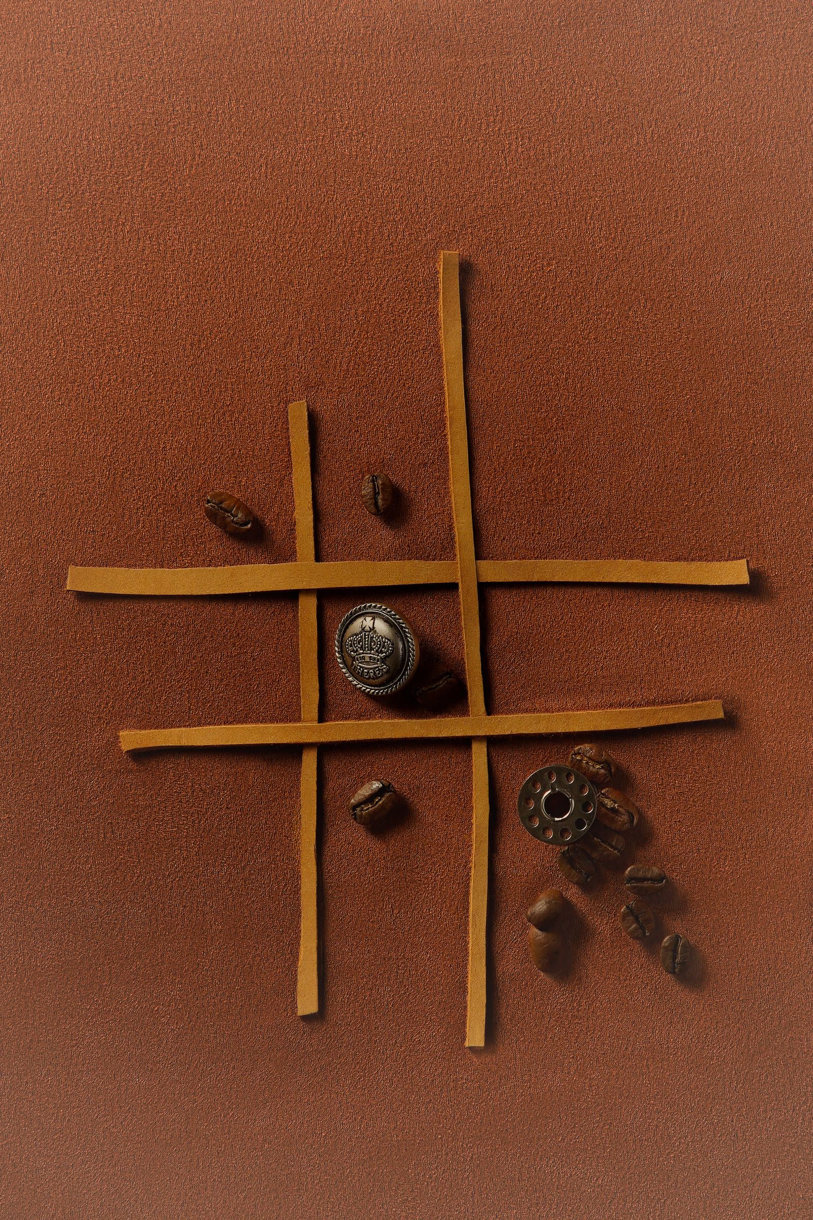 Leather strips laid in a grid on brown leather, with coffee beans, a button and a thread spool.